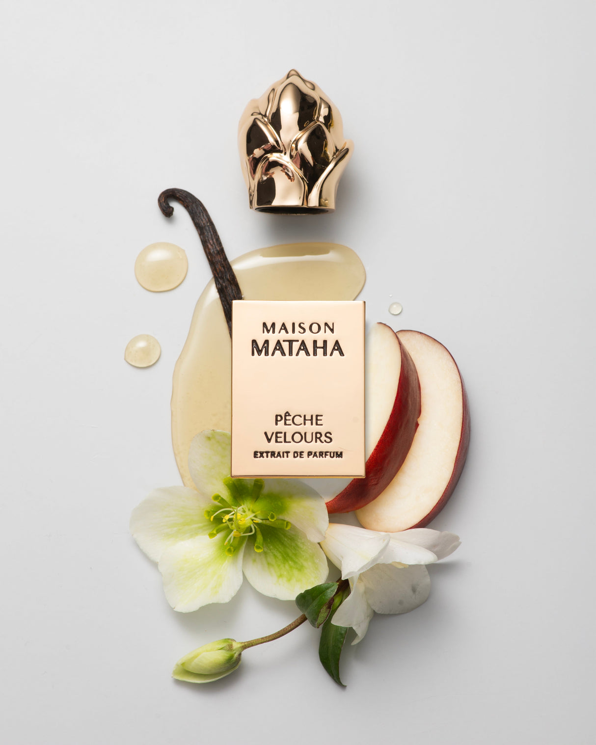 A gold Fragrapedia Haus Pêche Velours Extrait de Parfum bottle with its cap off, set among apple slices, vanilla bean, white flowers, petals, and droplets—capturing the allure of a velvety peach summer scent on a light gray background.
