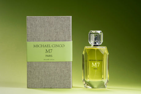 A bottle of M7 Eau de Parfum by Fragrapedia Haus with a faceted glass cap stands beside its textured grey box with a green label, both displayed against a green gradient background.