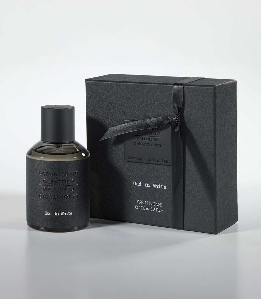 A black bottle of Oud in White Eau de Parfum by Fragrapedia Haus stands beside a matching ribbon-tied box, both with embossed labels—hinting at the floral blend of jasmine, oud, and sandalwood within.