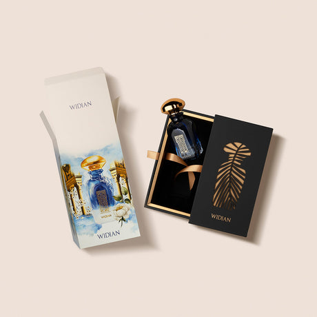 The Granada Extrait de Parfum by Fragrapedia Haus features a dark blue Widian bottle with a gold cap in a black and gold box with a ribbon, alongside outer packaging adorned with floral designs and the perfume bottle, evoking rose and juniper notes.