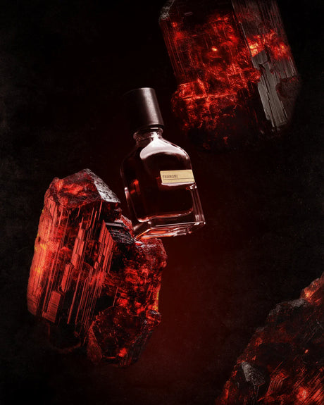 The Terroni Eau de Parfum by Fragrapedia Haus floats amid glowing red crystals on black, its dark bottle with black cap and gold label evoking the mysterious roots and dynamic energy of growth.