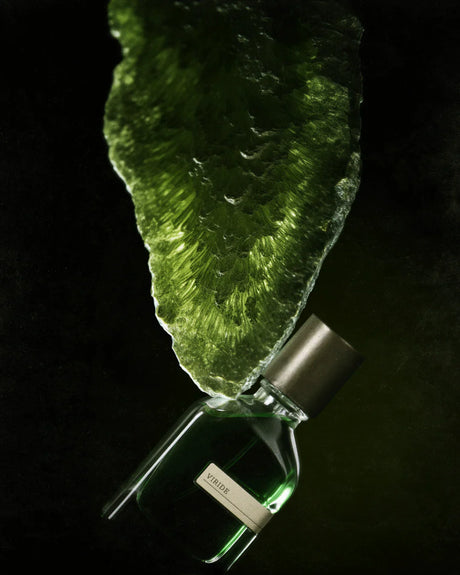 A green bottle of Viridi Eau de Parfum by Fragrapedia Haus rests beneath a textured green crystal, evoking herbal Yemeni traditions, all dramatically lit against a dark backdrop.