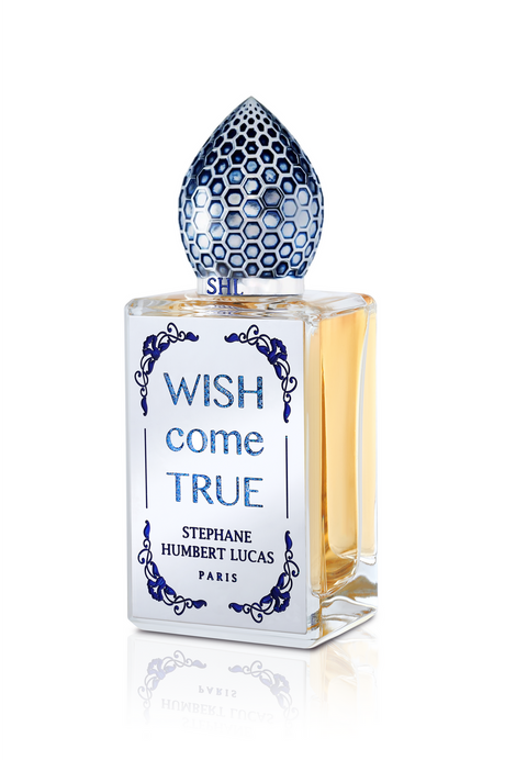 A clear glass bottle of Wish Come True Eau de Parfum by Fragrapedia Haus, shimmering with golden liquid and crowned by a blue and silver cap, evokes a magical allure and feminine essence.