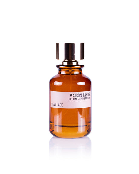A brown glass bottle with a shiny gold cap, labeled Maison Tahité Vanillade Eau de Parfum, suggests a citrus-floral scent with patchouli notes, set against a white background.