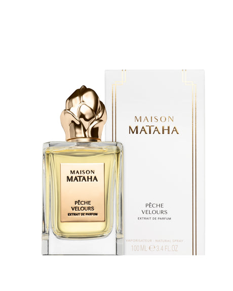 A 100ml bottle of Fragrapedia Haus Pêche Velours Extrait de Parfum by Maison Mataha, with a gold floral cap, sits before its white and gold box. This velvety peach scent is an ideal summer fragrance.