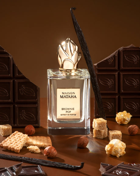 Brownie Pop Extrait de Parfum by Maison Mataha is pictured with chocolate squares, sugar cubes, vanilla beans, hazelnuts, biscuits, and caramelized popcorn—an irresistible gourmet scent for brownie fragrance lovers.