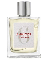 A clear glass perfume bottle with a silver cap, featuring a white label that reads ANNICKE 6 BY EIGHT & BOB in red and gray text. The liquid inside is light yellow.