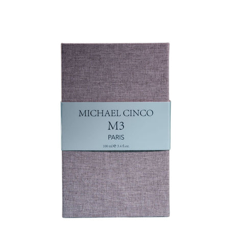A rectangular box with a textured lavender surface and a light gray label reading Fragrapedia Haus M3 Eau de Parfum 100 ml, suggesting a floral scent created by Michael Cinco with consciously sourced ingredients.