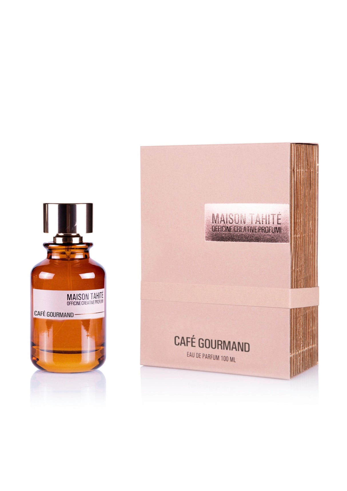 The amber-hued Café Gourmand Eau de Parfum by Maison Tahite, with a black and gold cap and branded label, sits beside its beige square box adorned with metallic accents. The scent features hazelnut coffee and amber dry notes.