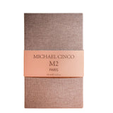 A rectangular box in textured beige with a peach band displays "M2 Eau de Parfum - Michael Cinco" by Fragrapedia Haus, 100 ml / 3.4 fl. oz., in elegant black font, reflecting a fragrance inspired by oriental spirituality.