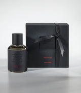 The Amberbomb Eau de Parfum by Laboratorio Olfattivo stands next to a sleek black gift box with red accents and subtle embossed text, both reflecting minimalist luxury on a light gray background.