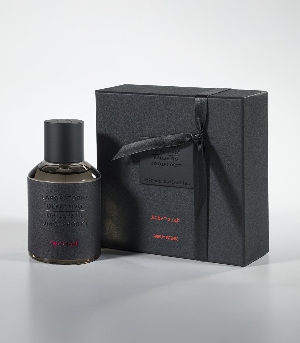 A bottle of Amberbomb Eau de Parfum by Laboratorio Olfattivo stands beside a black gift box with minimalist embossed text, both from the Extreme Collection of luxury fragrances.
