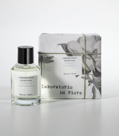 A bottle of Decou Vert Eau de Parfum by Laboratorio Olfattivo stands beside its floral-patterned box labeled "Laboratorio in Fiore." The scent combines vibrant florals with musky, woody notes; the bottle has a black cap and clear liquid.