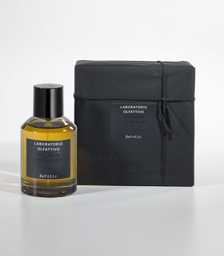 A bottle of Nerotic Eau de Parfum by Laboratorio Olfattivo with a black label stands beside its matching black box, wrapped in string on a white background, evoking the fragrance's unisex appeal and amber notes.