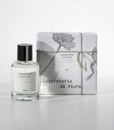 A glass bottle of Laboratorio Olfattivo's NUN Eau de Parfum stands beside a wrapped box with botanical designs, string, and matching branding, all set against a white background.