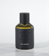 A bottle of Oud in White Eau de Parfum by Fragrapedia Haus, featuring a black cylindrical cap and textured dark gray label against a light background—an elegant floral fragrance with soft sandalwood notes.