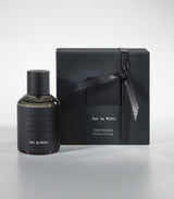 A bottle of Oud in White Eau de Parfum by Fragrapedia Haus sits beside its matching black ribbon-tied gift box, both arranged on a light gray surface.