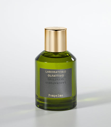 A green glass bottle of Pompelmo Eau de Parfum by Laboratorio Olfattivo, with a gold cap, rests on a light gray background. Its fragrance exudes the vibrant, bitter aroma of Italian citruses.