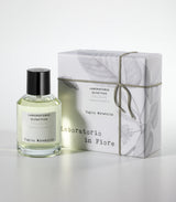 A bottle of Laboratorio Olfattivo's Tiglio Mirabilis Eau de Parfum stands beside its illustrated box, tied with string; the fragrance fuses spicy and floral notes atop a woody musky base.