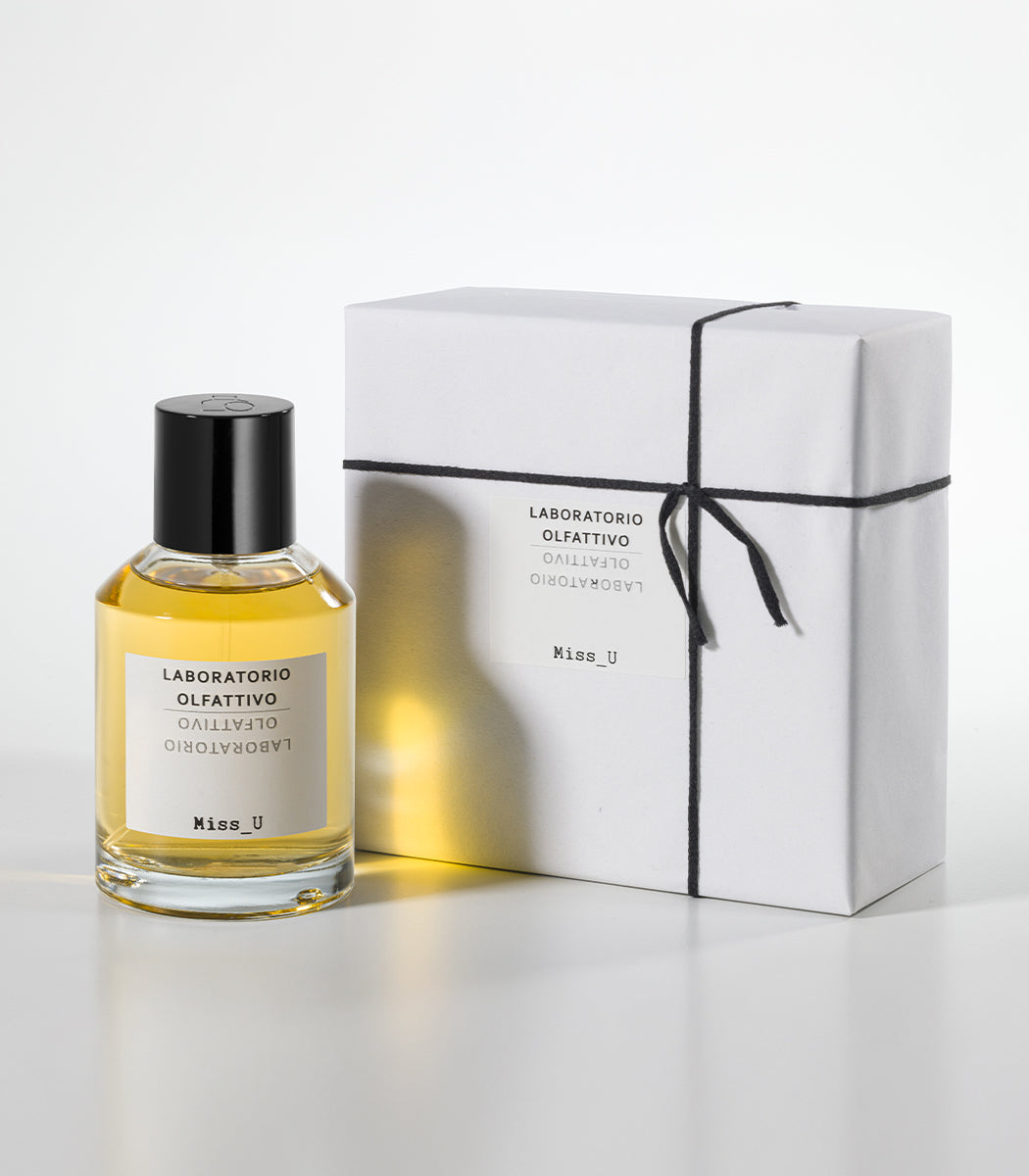 A bottle of MISS U Eau de Parfum by Laboratorio Olfattivo sits beside a white, neatly wrapped box tied with black string on a plain white background.