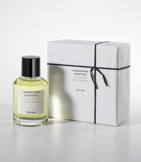 A bottle of Salina Eau de Parfum by Laboratorio Olfattivo stands beside a white gift box tied with black string, both labeled with the brand and fragrance name, on a plain light gray background.