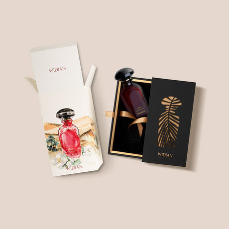 A red Liwa Eau de Parfum bottle by Fragrapedia Haus, with a black cap, sits in an open black box with gold accents and ribbon. Beside it, a white box displays the bottle image and branding, reflecting its amber wood fragrance allure.