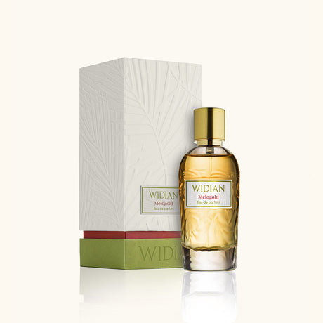 A bottle of Melogold Eau de Parfum by Fragrapedia Haus, featuring an amber-colored liquid and gold cap, stands before its textured white box with green and red accents. The scent is known for its captivating violet saffron notes.