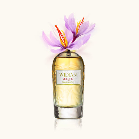 A bottle of Melogold Eau de Parfum by Fragrapedia Haus, adorned with delicate purple flowers and orange stamens atop, set against a light neutral background—an homage to its violet saffron scent.