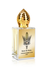 A rectangular perfume bottle with a gold honeycomb cap and pale yellow liquid, labeled Rose de Petra Eau de Parfum by Fragrapedia Haus, captures the elegance of Bulgarian Rose in this refined Stephane Humbert Lucas fragrance.