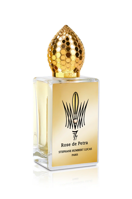 A rectangular perfume bottle with a gold honeycomb cap and pale yellow liquid, labeled Rose de Petra Eau de Parfum by Fragrapedia Haus, captures the elegance of Bulgarian Rose in this refined Stephane Humbert Lucas fragrance.