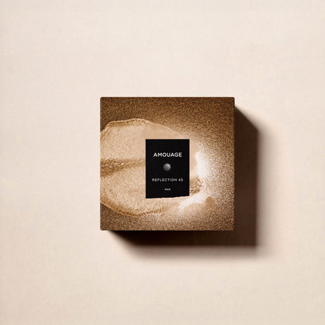 A square, brown, textured box of Reflection 45 Man Extrait de Parfum by Fragrapedia Haus sits on a light beige surface, shadow to the right. Its black label with white text hints at the woody floral musk fragrance inside.