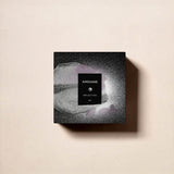 A square black box of Fragrapedia Haus Reflection Man Eau de Parfum rests on a beige surface, its textured design and centered branding reflecting the timeless elegance of this masculine fragrance.