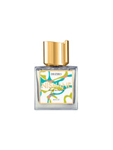 A square glass perfume bottle with a gold cap and an abstract yellow, green, and blue label reading "Deziro Extrait de Parfum - Nishane" by Fragrapedia Haus evokes the vibrant freshness of vetiver. The background is white.