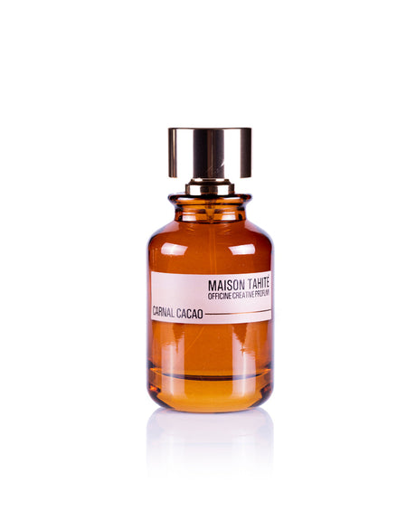 A brown glass perfume bottle with a shiny gold cap, labeled Carnal Cacao Eau de Parfum by Maison Tahite, sits on a white background and features notes of Cocoa Absolute and Tuberose Absolute.