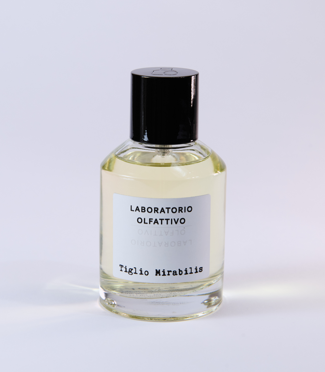 A clear glass bottle of Tiglio Mirabilis Eau de Parfum by Laboratorio Olfattivo, accented with a black cap and label, evokes floral and spicy notes and is photographed against a plain white background.